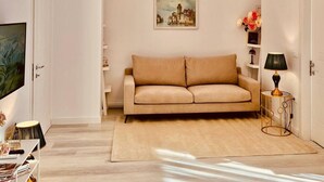 A living room with a beige sofa, a painting on the wall, a lamp, and a TV on the left. - Leo s Garden View Apartment Cozy 1BR (Tirana)