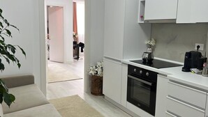 A modern kitchen with white cabinets, a stove, and a coffee maker. - Leo s Garden View Apartment Cozy 1BR (Tirana)