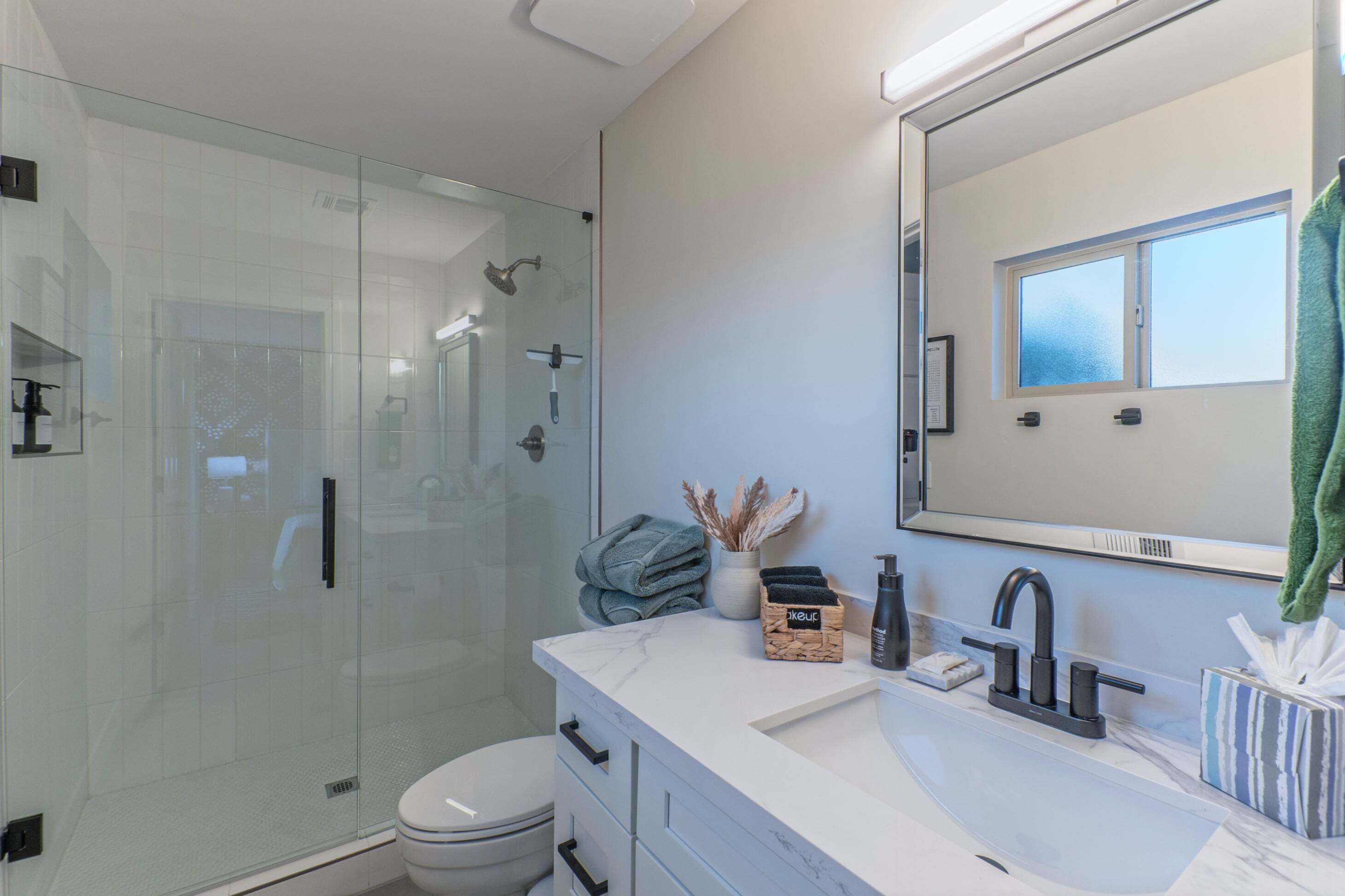 A modern bathroom with a glass-enclosed shower, a white sink with a marble countertop, and a large mirror.