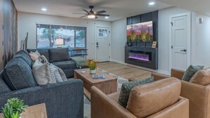 A modern living room with a grey sofa, a brown leather sofa, a coffee table, a fireplace, and a ceiling fan. - Fountain Hills Splendor: One Story, Pvt Pool, Putting Green, Fire Pit, Near Hiking/Biking & Golf (Fountain Hills)