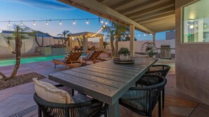 An outdoor patio with a wooden table and chairs, string lights, and a pool. - Fountain Hills Splendor: One Story, Pvt Pool, Putting Green, Fire Pit, Near Hiking/Biking & Golf (Fountain Hills)