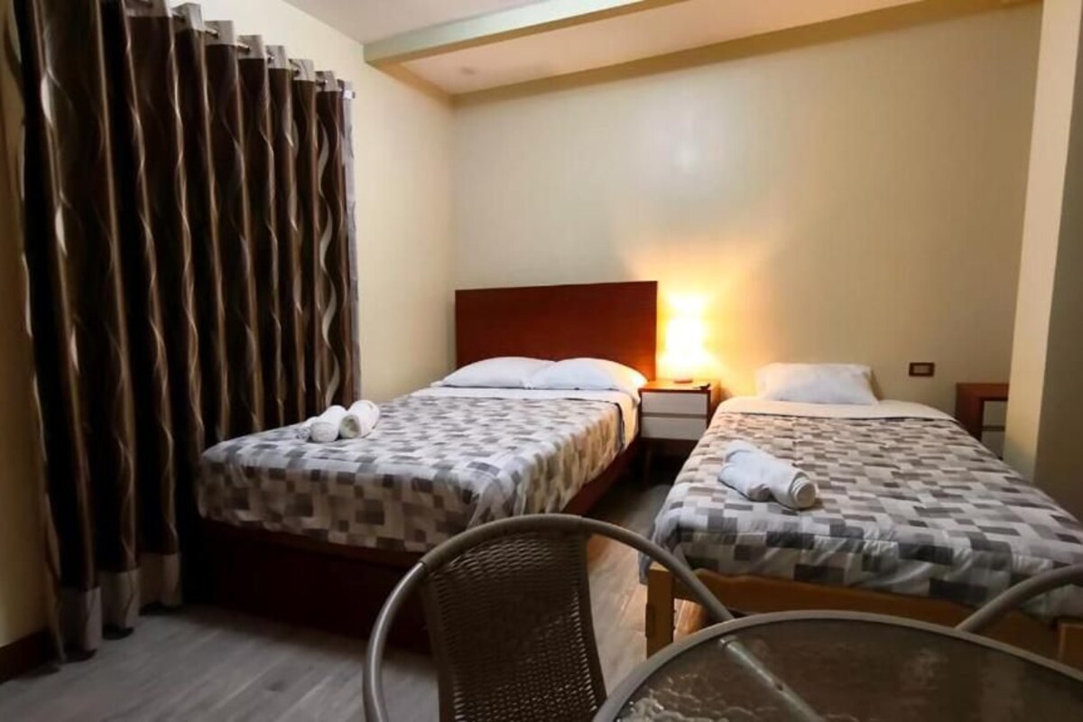 Quarto de hotel com duas camas, uma mesa e uma cadeira.