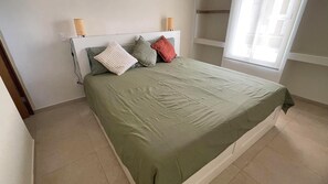 A bed with a green bedspread, two bedside lamps, and a window with blinds.