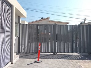 A gated area with a metal fence, a red and white traffic cone, and a building with a closed shutter door.
