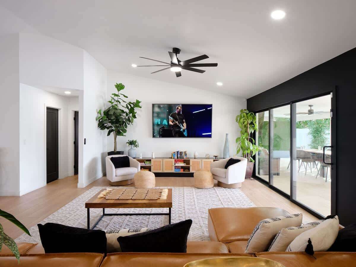 Una sala de estar moderna con un ventilador de techo, un televisor de pantalla plana y un ventanal grande.
