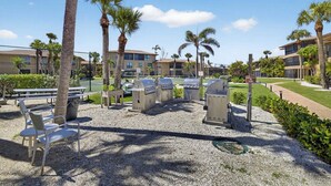 A patio area with barbecue grills, outdoor seating, and palm trees. - Blind Pass Condos at Bowman's Beach E202 on beautiful Sanibel Island (Sanibel)