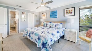 A bedroom with a bed, a ceiling fan, a nightstand, a chair, and artwork on the walls. - Blind Pass Condos at Bowman's Beach E202 on beautiful Sanibel Island (Sanibel)