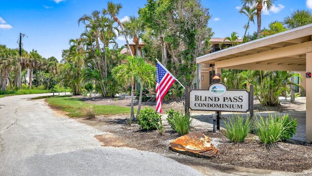 A sign for a condominium with an American flag, surrounded by palm trees and a building with a covered entrance. - Blind Pass Condos at Bowman's Beach E202 on beautiful Sanibel Island (Sanibel)