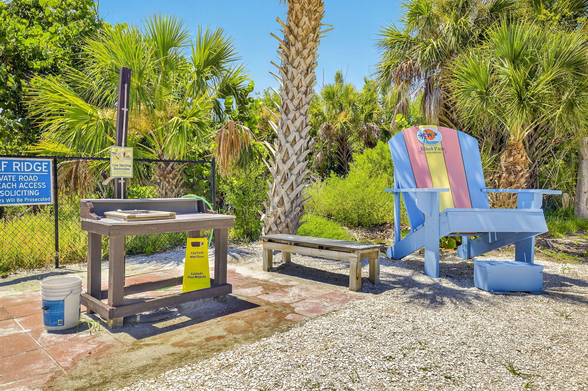 Area spiaggia con cartello che indica accesso riservato, una panchina in legno, una sedia da spiaggia e un tavolo con indicazione di una fontanella.
