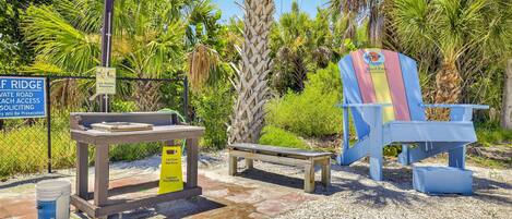Area spiaggia con cartello che indica accesso riservato, una panchina in legno, una sedia da spiaggia e un tavolo con indicazione di una fontanella.
