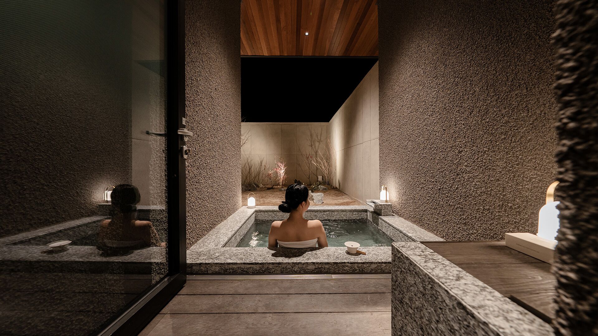 Een wellnessruimte met een stenen muur, een houten plafond en iemand in een bad.