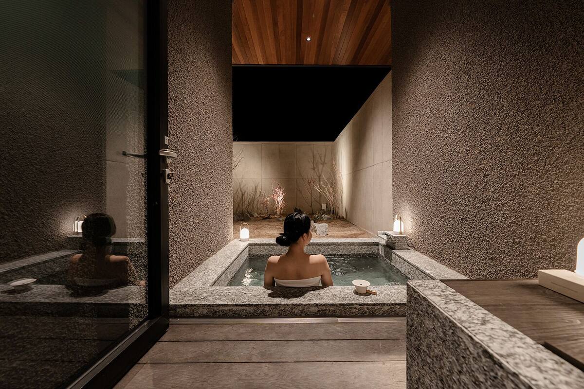 Un espace de bien-être avec un mur en pierre, un plafond en bois et une personne dans une baignoire.