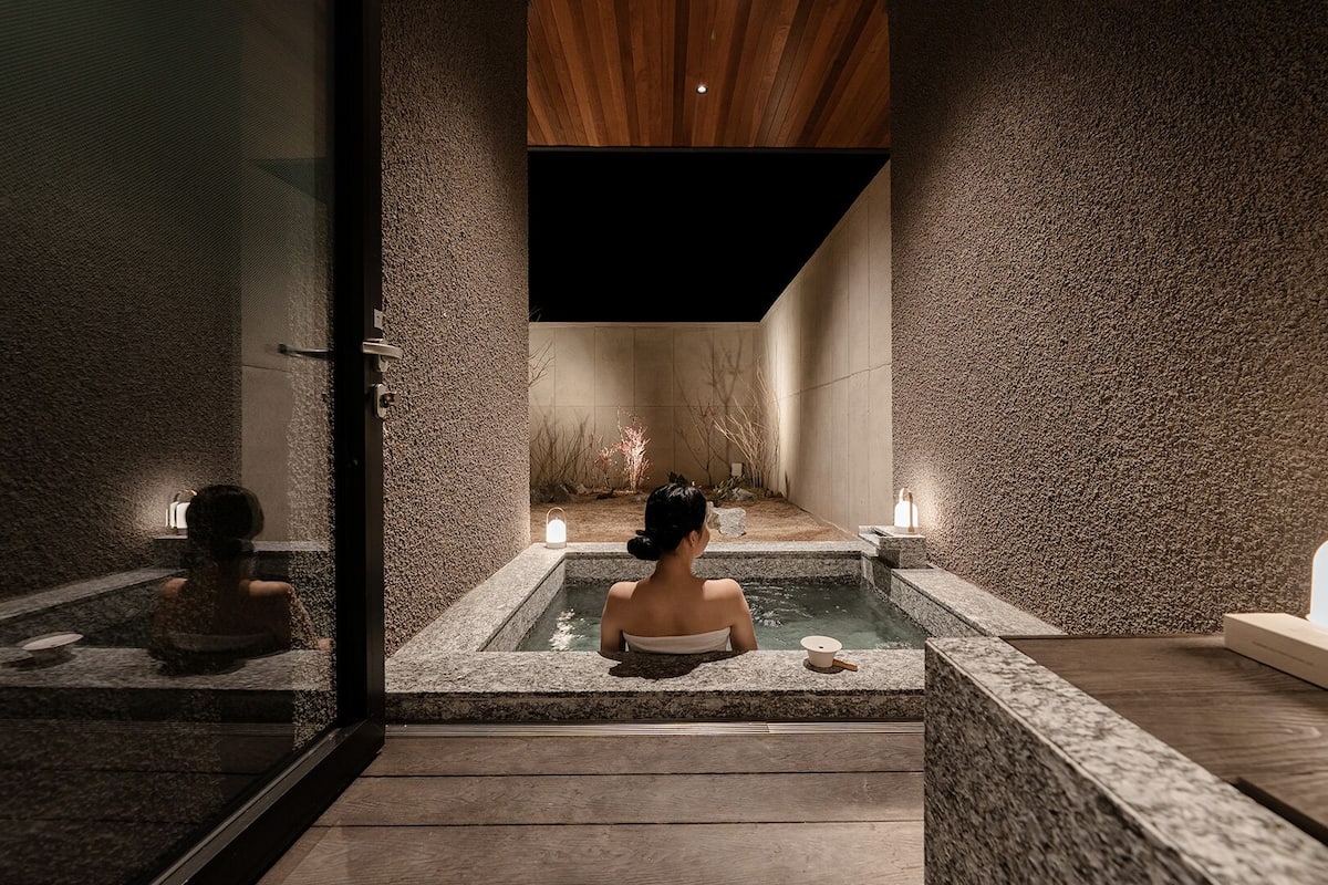 A spa area with a stone wall, a wooden ceiling, and a person in a bathtub.