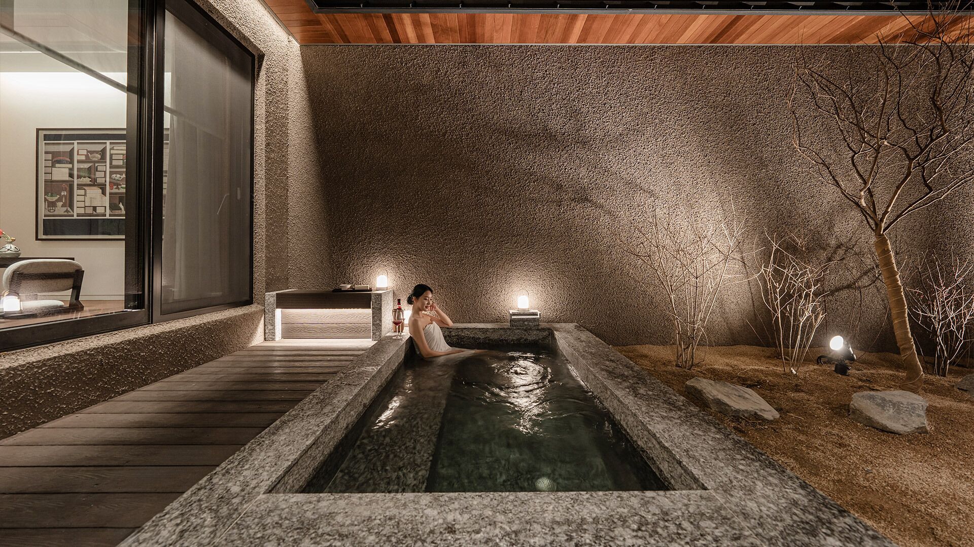 Een wellnessruimte met een whirlpool, houten terras en stenen muren.