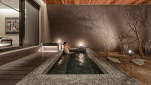 Een wellnessruimte met een bubbelbad, houten terras en een stenen muur.