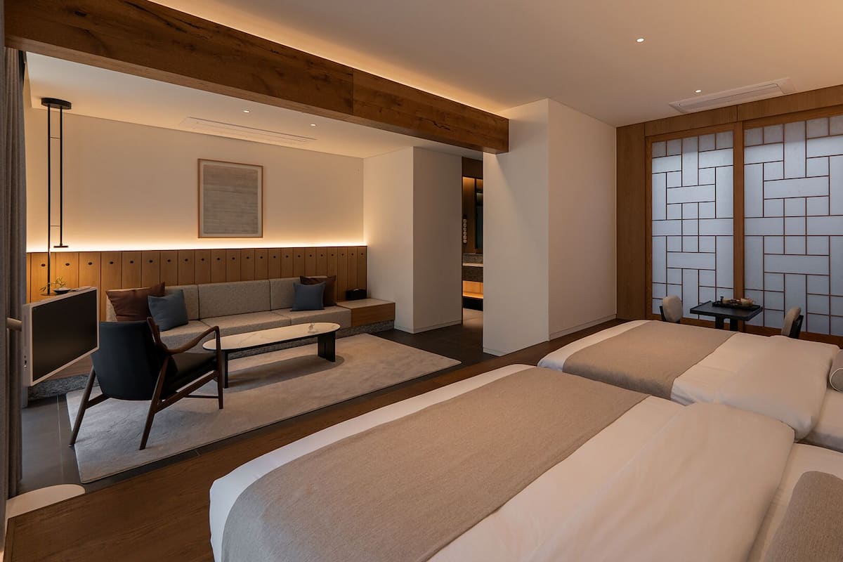Une chambre d’hôtel moderne équipée d’un canapé, de deux lits, d’un bureau et offrant une vue sur un paravent japonais traditionnel.