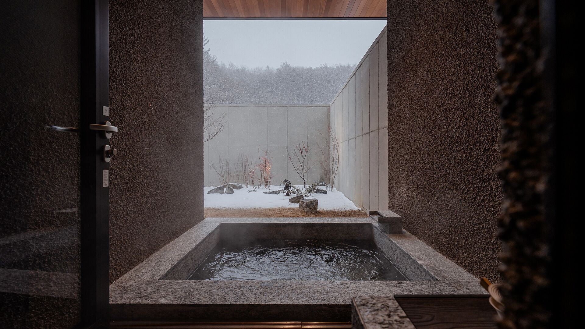 Een warmwaterbronbad met uitzicht op een besneeuwd landschap door een houten raam.