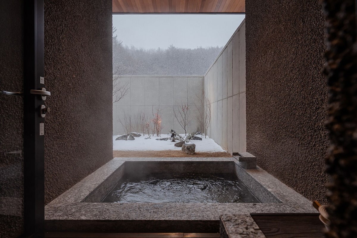 A hot spring bath with a view of a snowy landscape through a wooden-framed window.