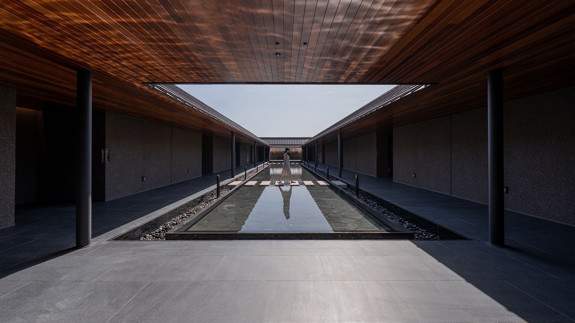 A modern building with a central reflective water feature, wooden ceiling, and a symmetrical design.