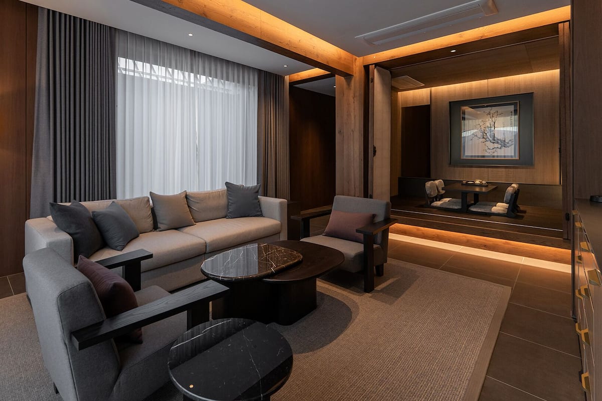 A modern hotel room with a sofa, armchairs, a coffee table, and a dining area.