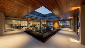 Um interior moderno com piscina central, paredes de vidro e teto de madeira.