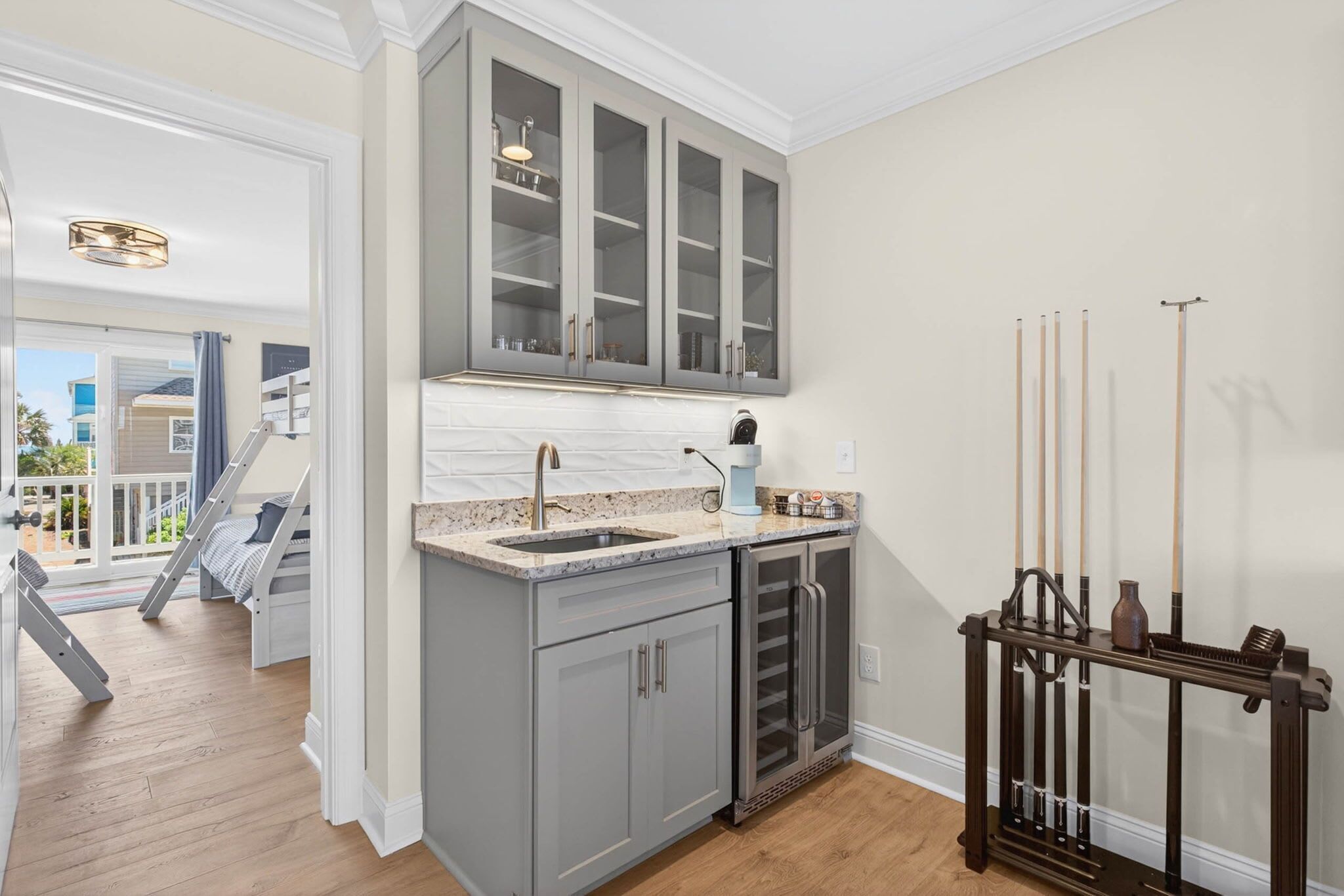 A kitchen with grey cabinets, a sink, and a wooden rack holding pool cues.