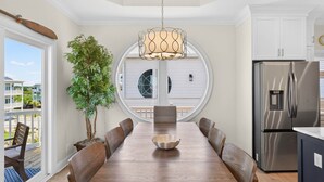 Een eetkamer met een houten tafel, stoelen, een kroonluchter, een potplant en uitzicht door een raam.
