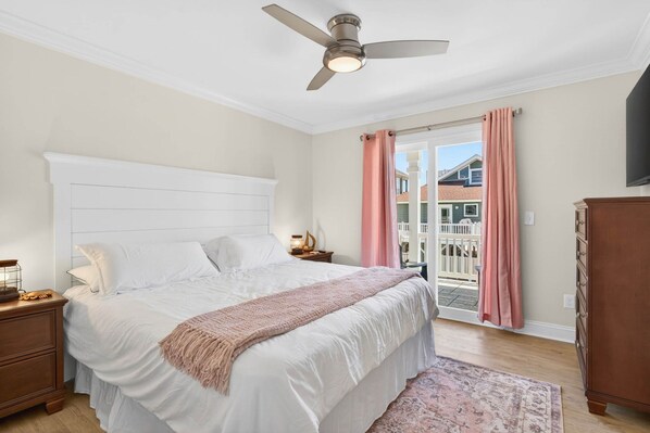 Quarto com cama, mesa de cabeceira, cômoda, ventilador de teto e vista para um muro branco e edifícios lá fora.