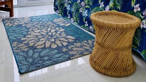 Une pièce comprenant un lit, une chaise, un tabouret en osier, une grande fenêtre avec des rideaux et une vue sur la mer.