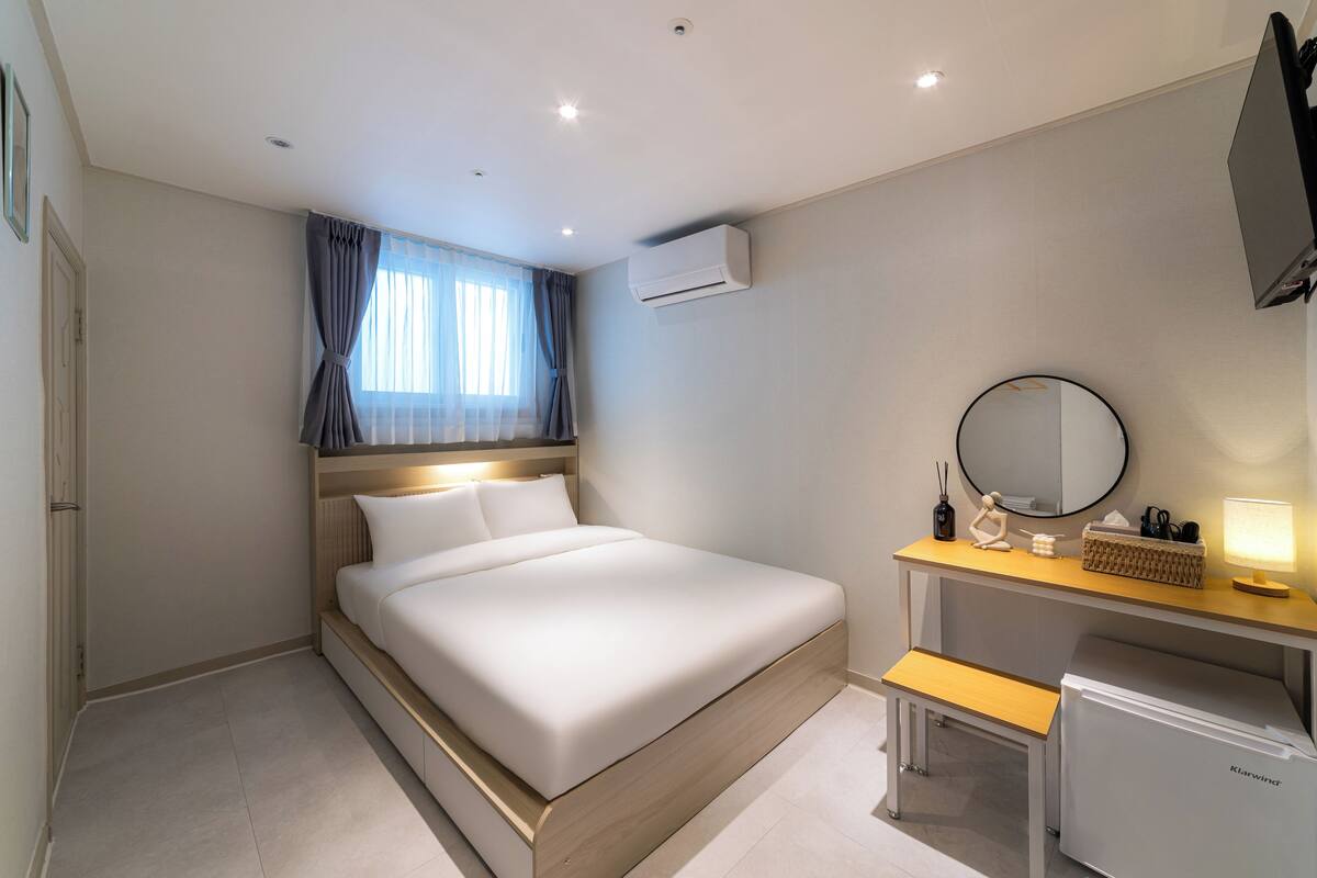 A modern hotel room with a bed, desk, and built-in air conditioning unit.