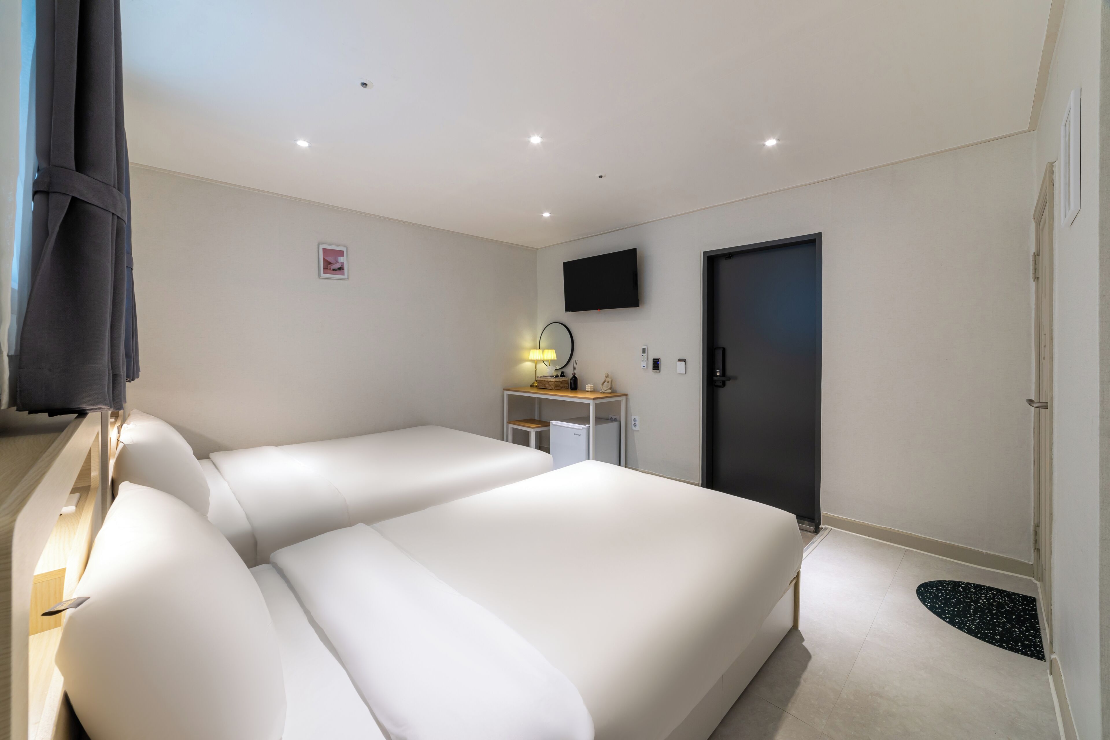 A hotel room with a large bed, a desk with a lamp, a TV, and a door.
