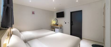 A hotel room with a large bed, a desk with a lamp, a TV, and a door.