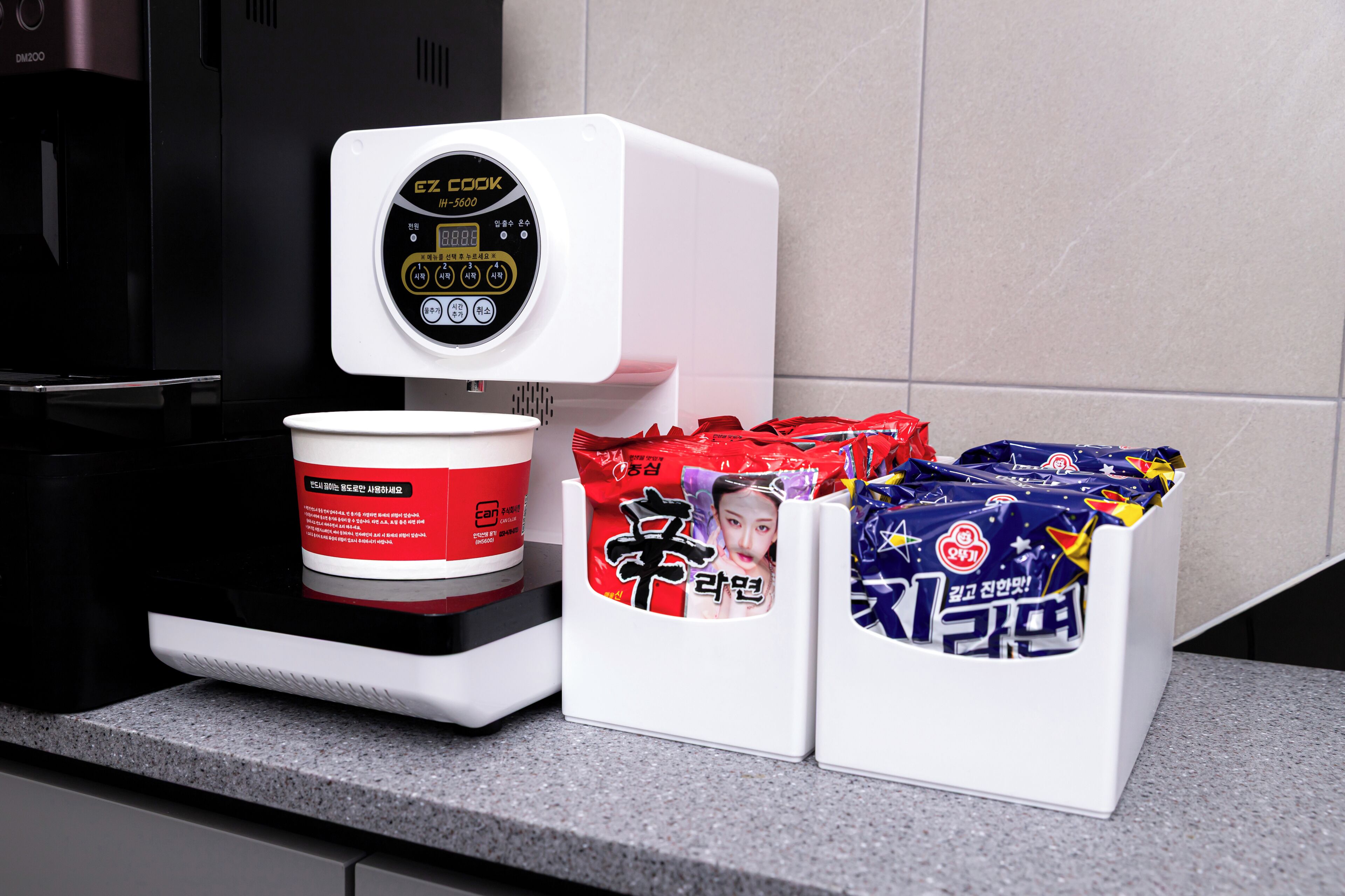 A kitchen area with a coffee maker, a white container, and two white boxes with Korean text.