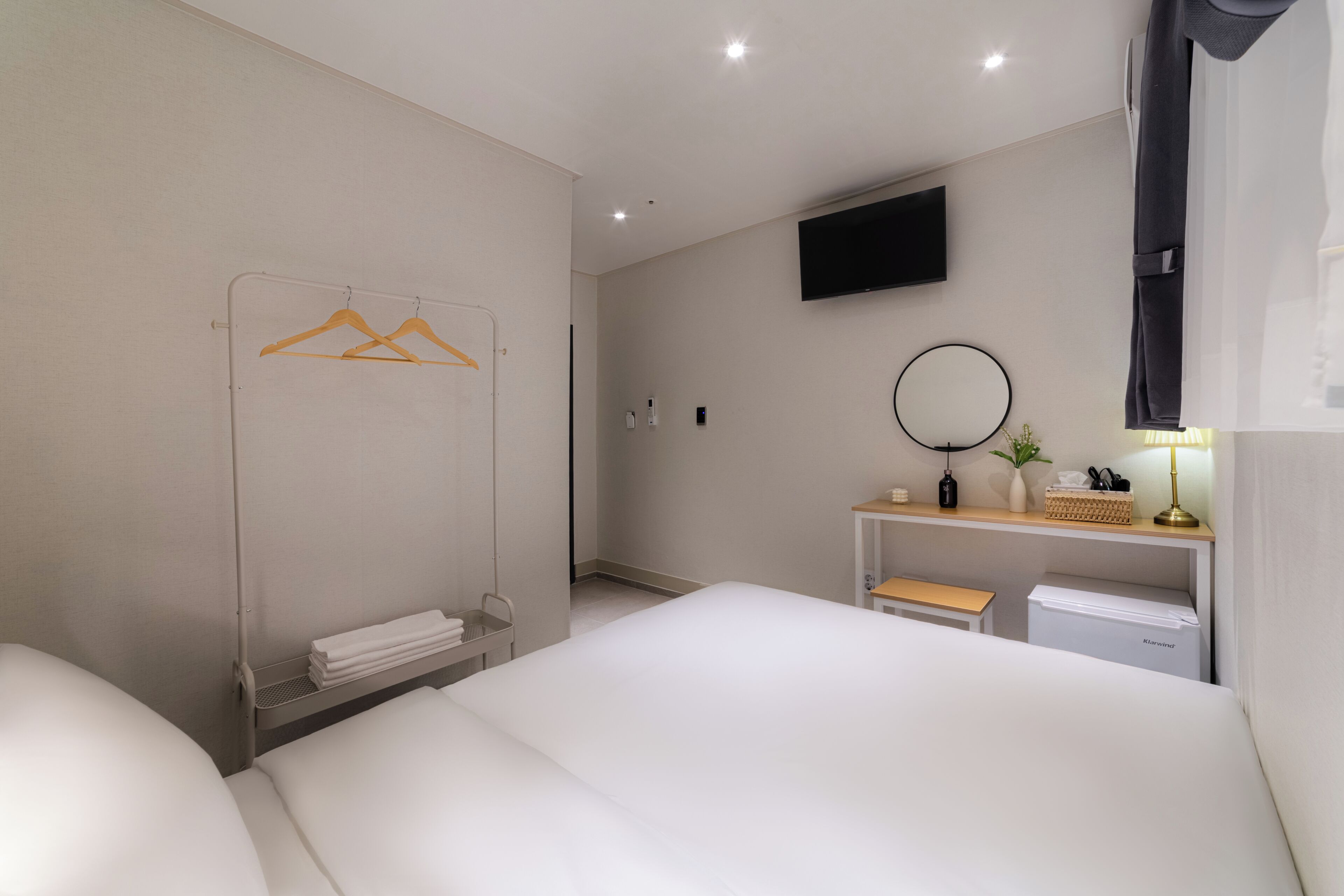 Une chambre d’hôtel moderne équipée d’un lit, d’un téléviseur fixé au mur, d’une table de chevet avec une lampe et d’un petit coin salon.