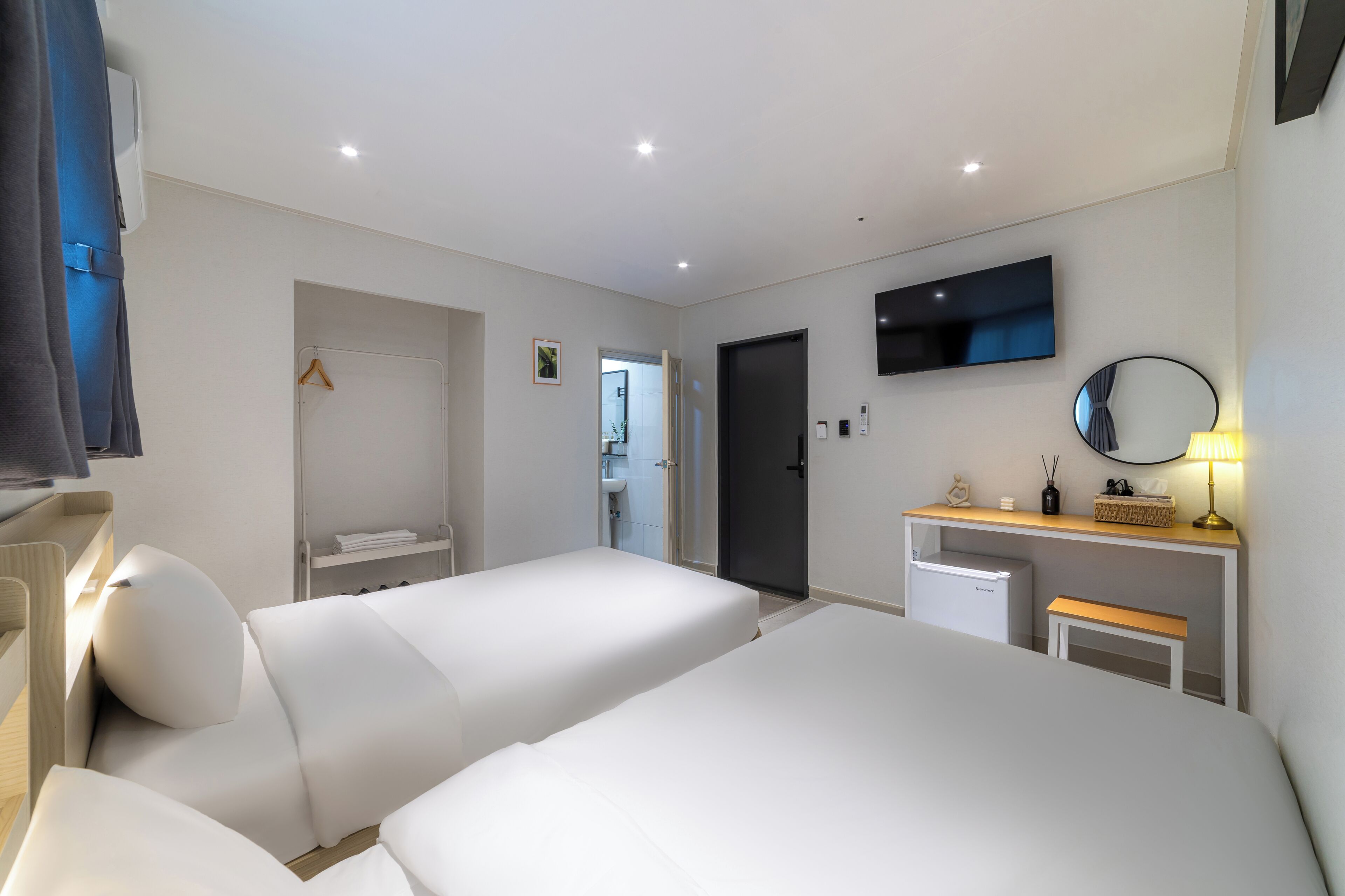 Une chambre d’hôtel avec deux lits, une télévision, un bureau avec une lampe, un miroir et un petit réfrigérateur.