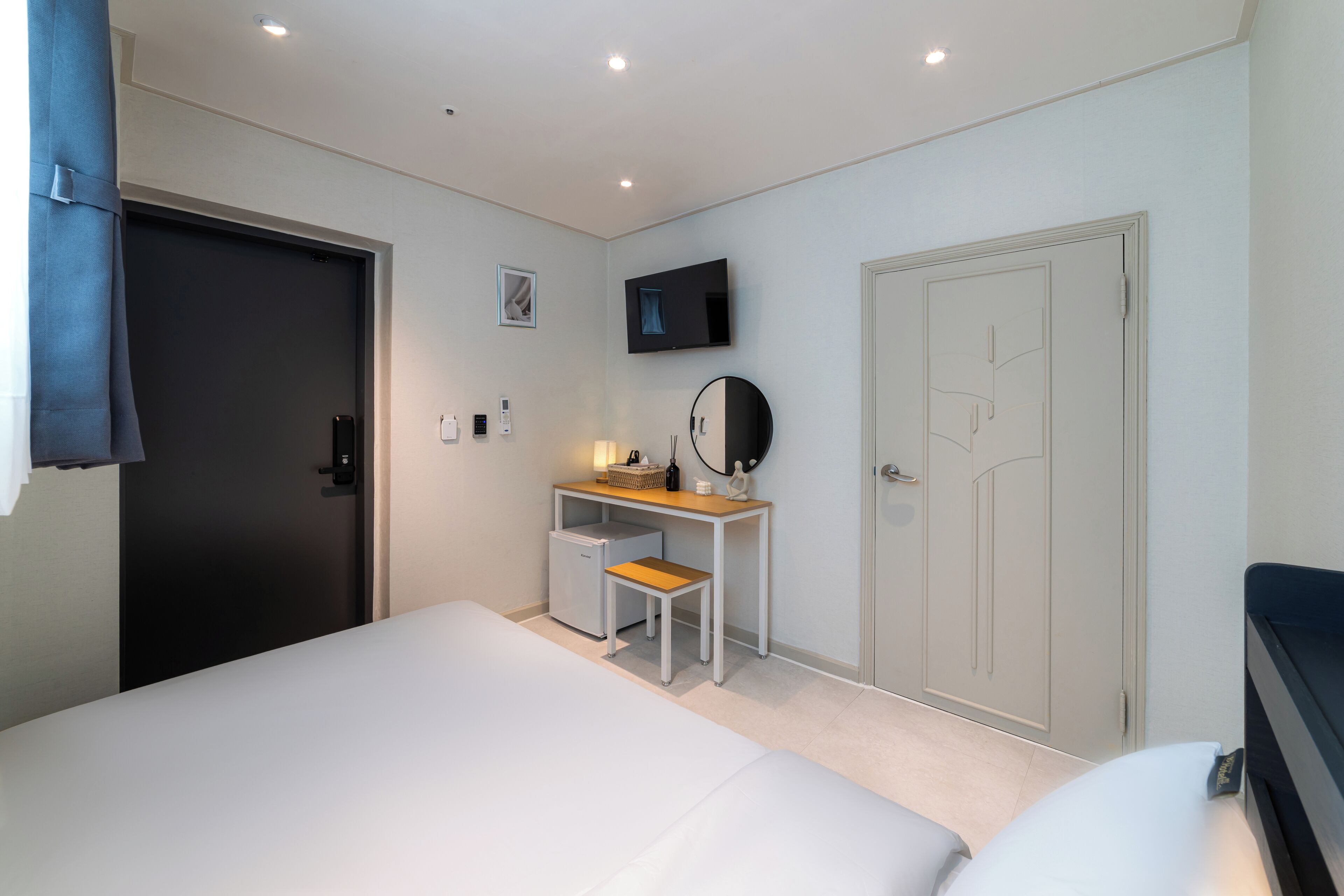Un dormitorio con cama, escritorio, silla, televisor y puerta.