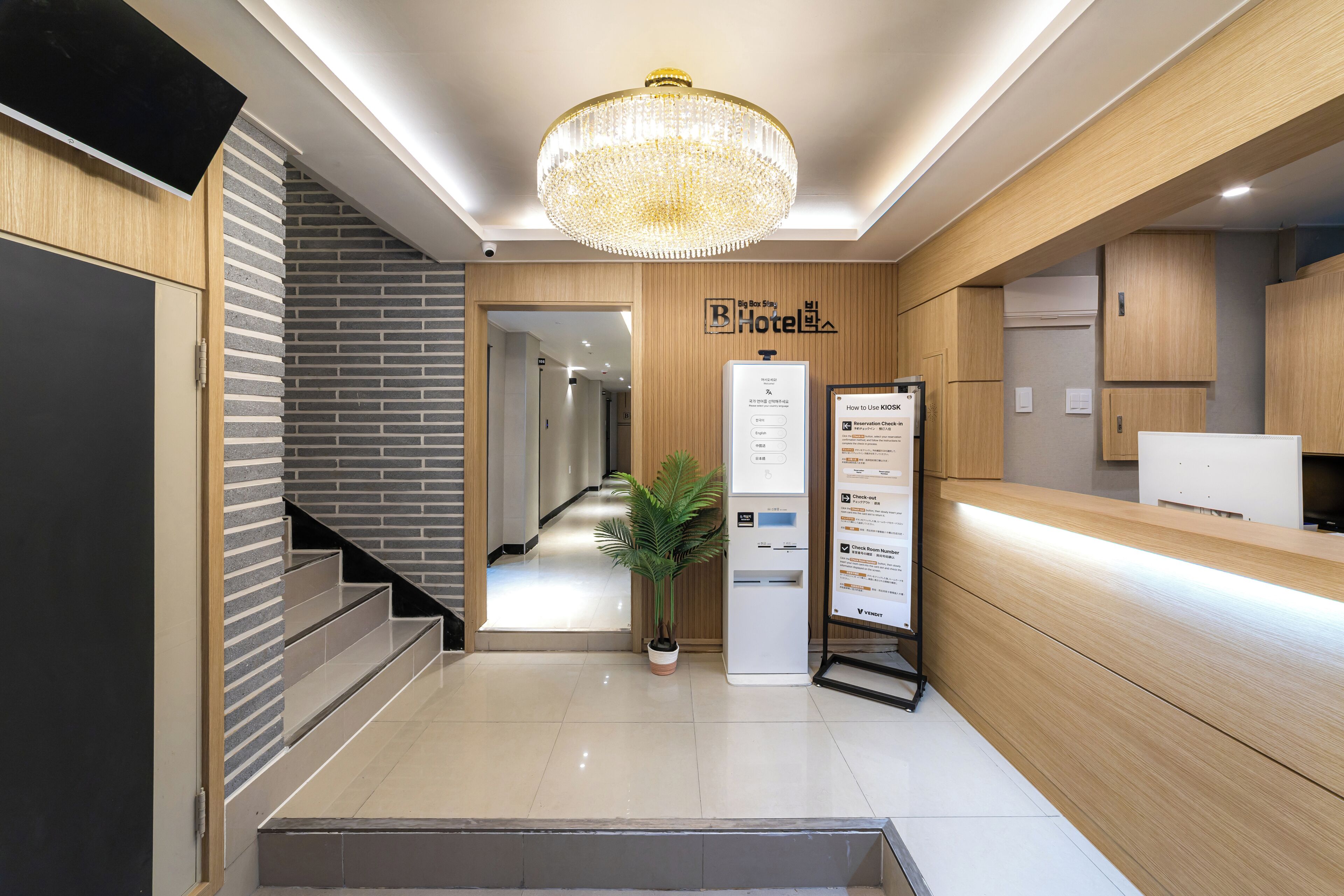 A hotel reception area with a modern design, a staircase, a reception desk, and a chandelier.