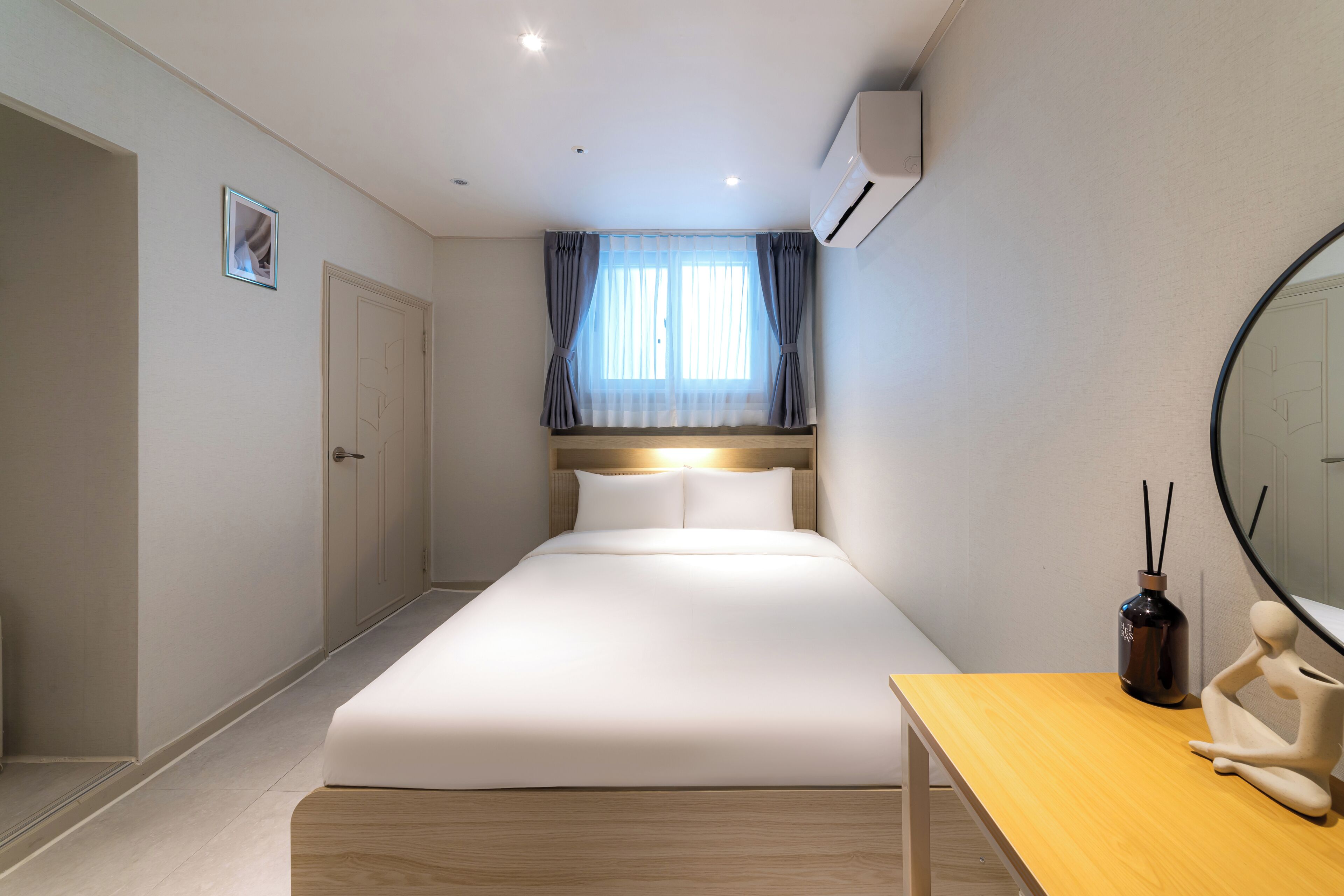 Una camera d'albergo moderna con un letto, un comodino in legno, uno specchio e un condizionatore d'aria.
