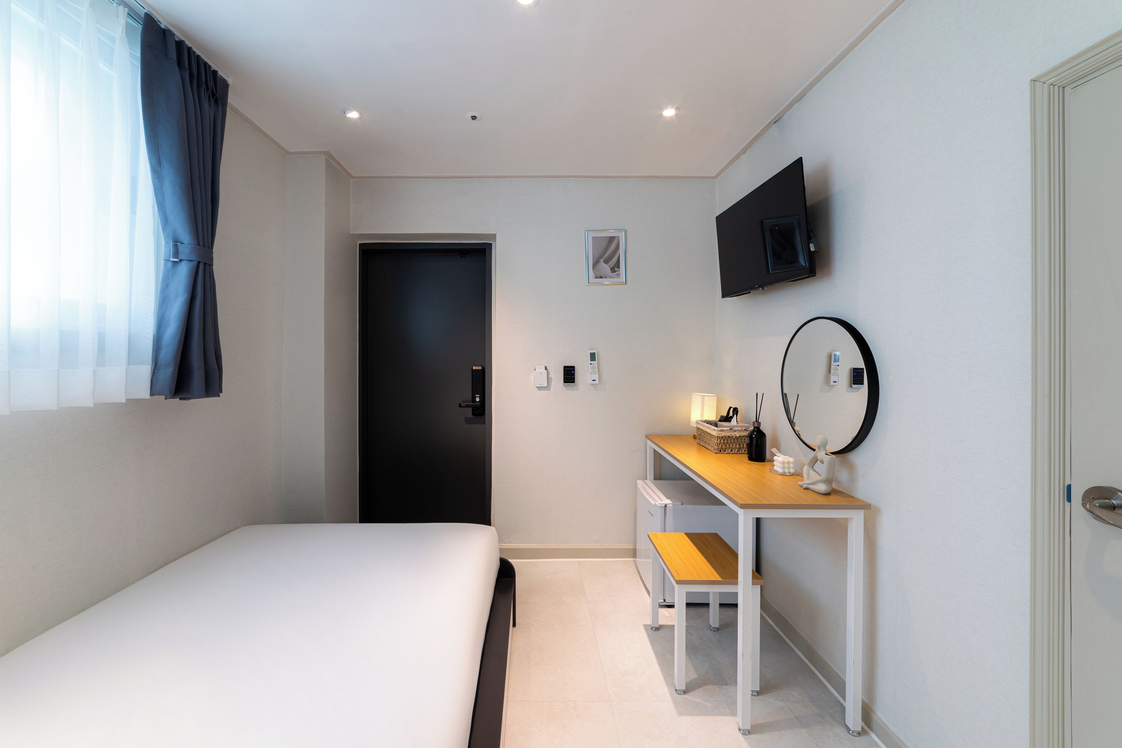 A bedroom with a bed, a desk, a chair, a TV, and a door.