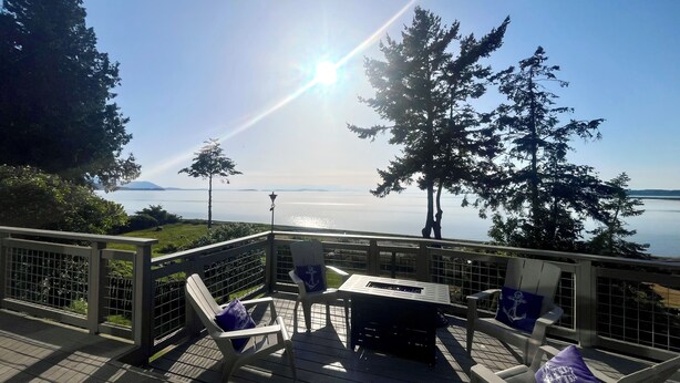 A deck with chairs and a table, overlooking a body of water and trees. - Private Beach Front Executive Home (Bellingham)