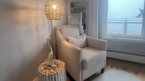 A room with a light-colored armchair, a woven floor lamp, a round rug, and a window with a view. - Private Beach Front Executive Home (Bellingham)
