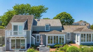 A two-story house with a balcony, a covered porch, and a fenced garden area. - Blue Tide Retreat Steps from Private Beach (Mashpee)