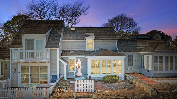 A two-story house with a porch, a small garden, and a stone wall. - Blue Tide Retreat Steps from Private Beach (Mashpee)