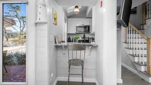 A narrow kitchen with white walls, a stainless steel microwave, and a small bar stool. - Blue Tide Retreat Steps from Private Beach (Mashpee)
