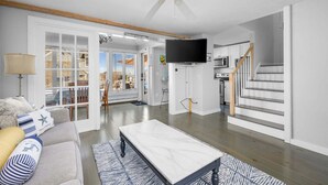 A spacious living room with a ceiling fan, a flat-screen TV, a sofa, and a dining area. - Blue Tide Retreat Steps from Private Beach (Mashpee)