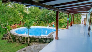 Ein überdachter Pool mit Steinmauern, umgeben von üppigem Grün und einer Holzpergola.