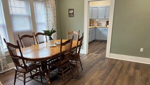 Een eetgedeelte met een houten tafel en stoelen, een potplant en een keuken op de achtergrond.