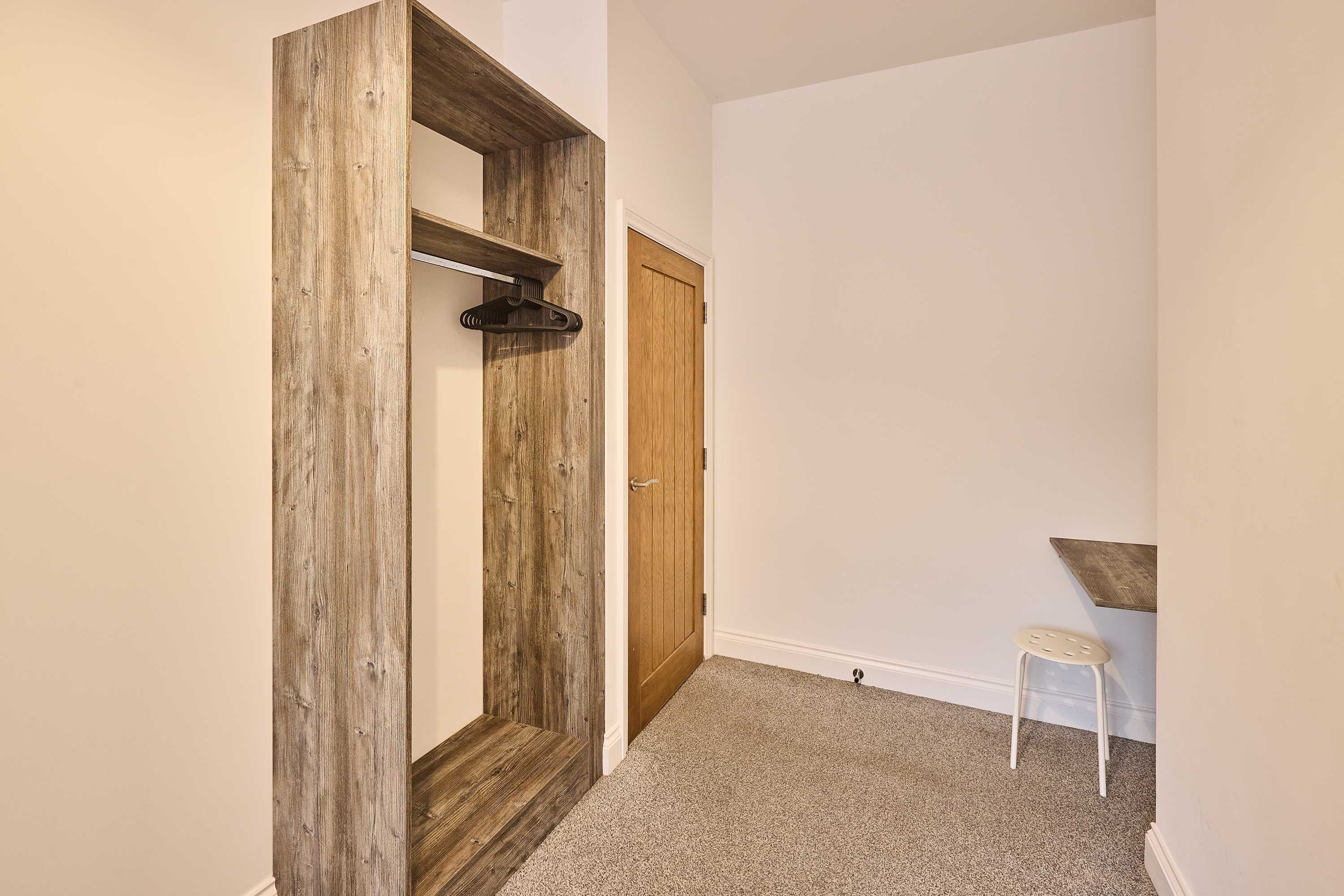 A hallway with a wooden door, a coat rack, and a small white stool.