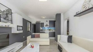 A modern living room with a sofa, coffee table, and TV. A kitchen is visible in the background. - Holiday apartment with air conditioning (Novigrad)