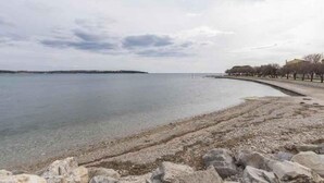 A coastal area with a clear water body, rocky shoreline, and a distant building. - Holiday apartment with air conditioning (Novigrad)